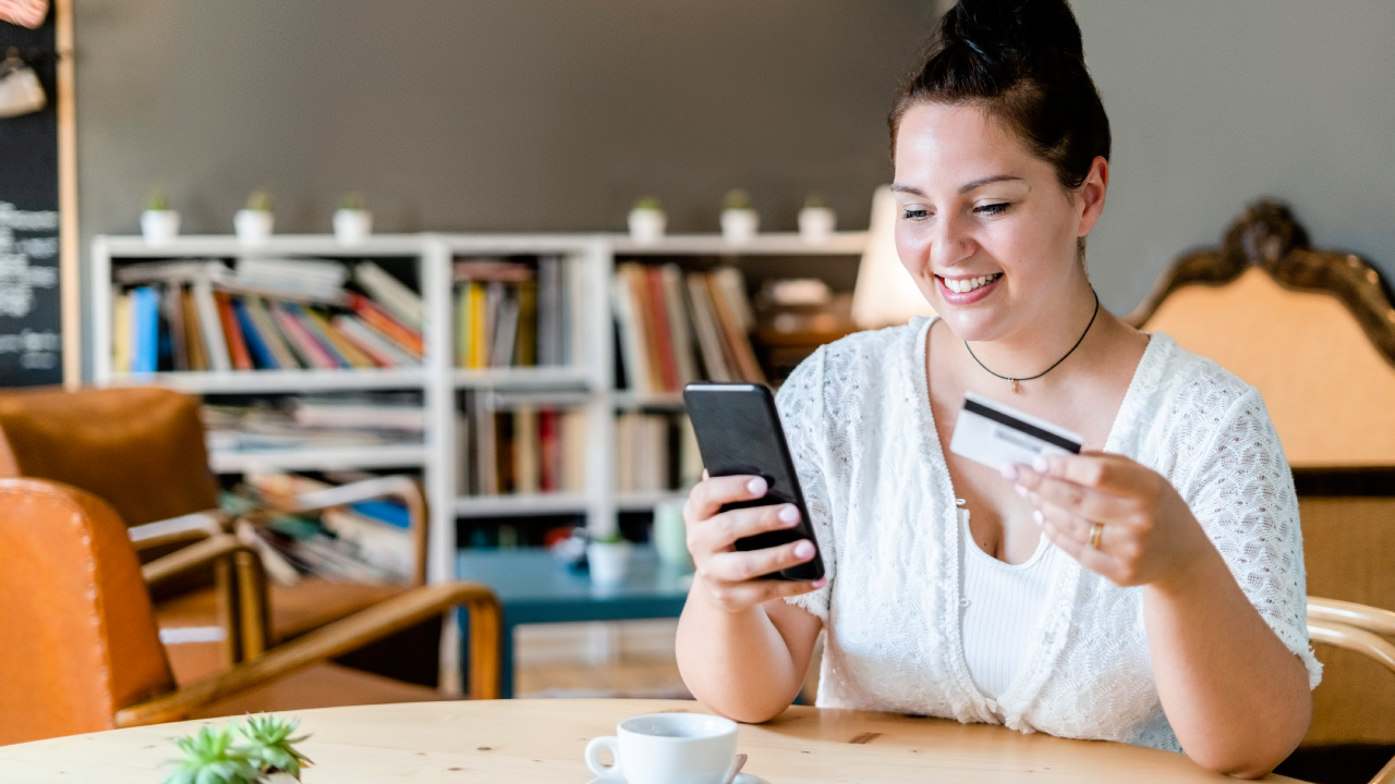 Smiling woman with coffee on table doing online shopping over mobile phone in cafe - stock photo