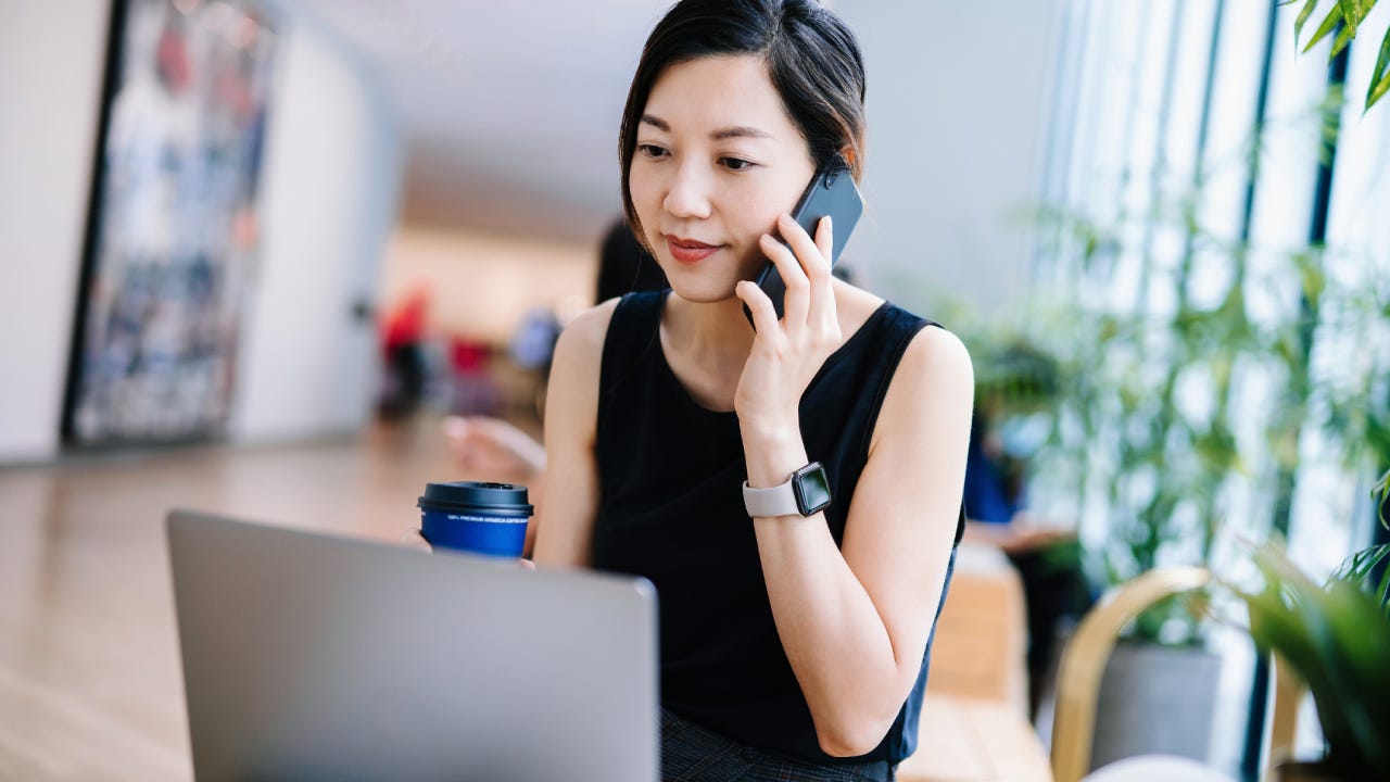 businesswoman working in a modern office space, working on laptop and taking a phone call at her desk