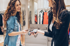 Young woman giving her credit card for a contactless payment in the fashion store