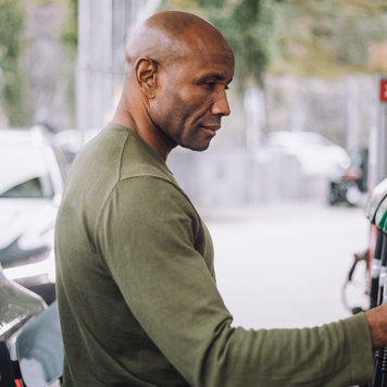 Side view of mature man doing payment through credit card while standing at gas station - stock photo