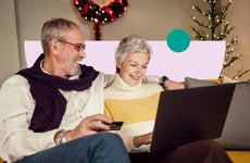 design image of an elderly couple smiling while sitting together on a couch and looking at a laptop