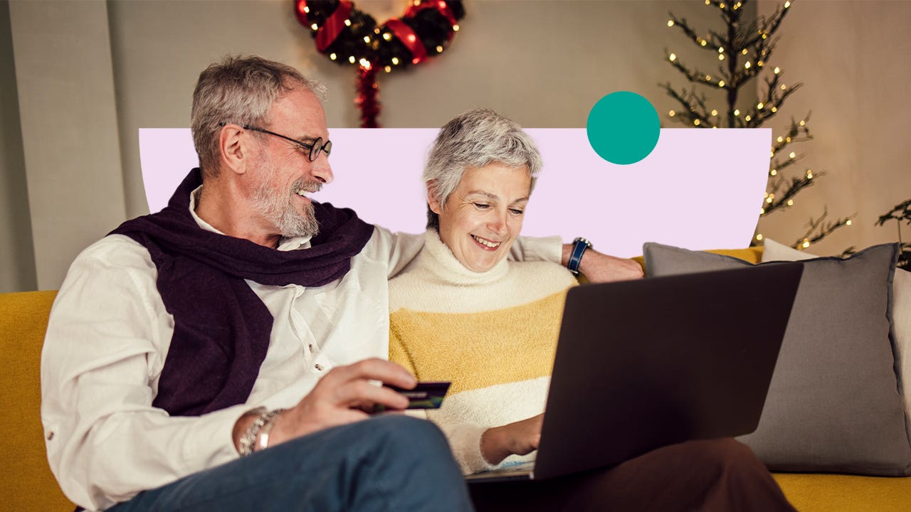 design image of an elderly couple smiling while sitting together on a couch and looking at a laptop