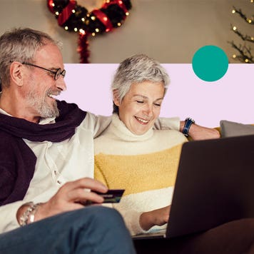 design image of an elderly couple smiling while sitting together on a couch and looking at a laptop