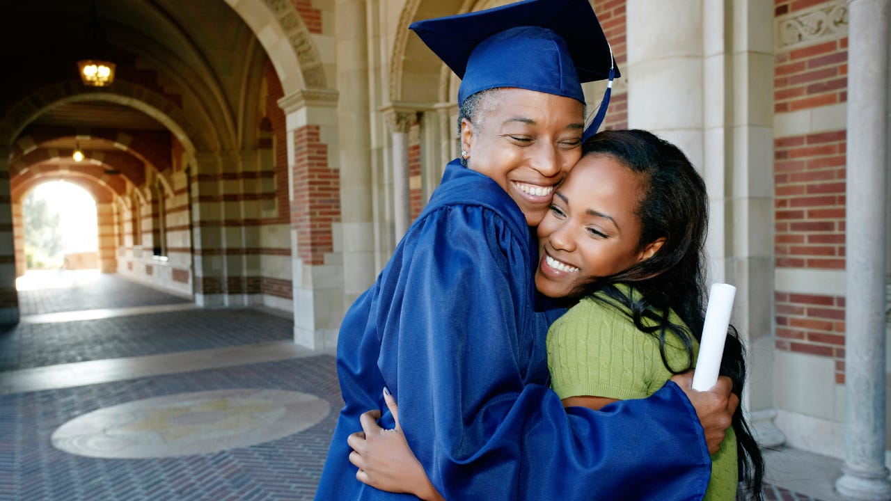 woman holding graduation diploma and hugging daughter