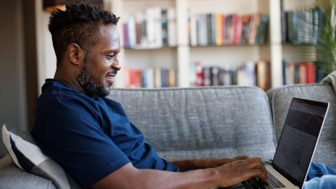 Relaxed smiling man sitting on sofa and using laptop