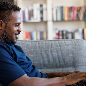 Relaxed smiling man sitting on sofa and using laptop