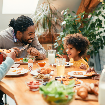Happy black parents and their kids talking while having breakfast together in dining room.