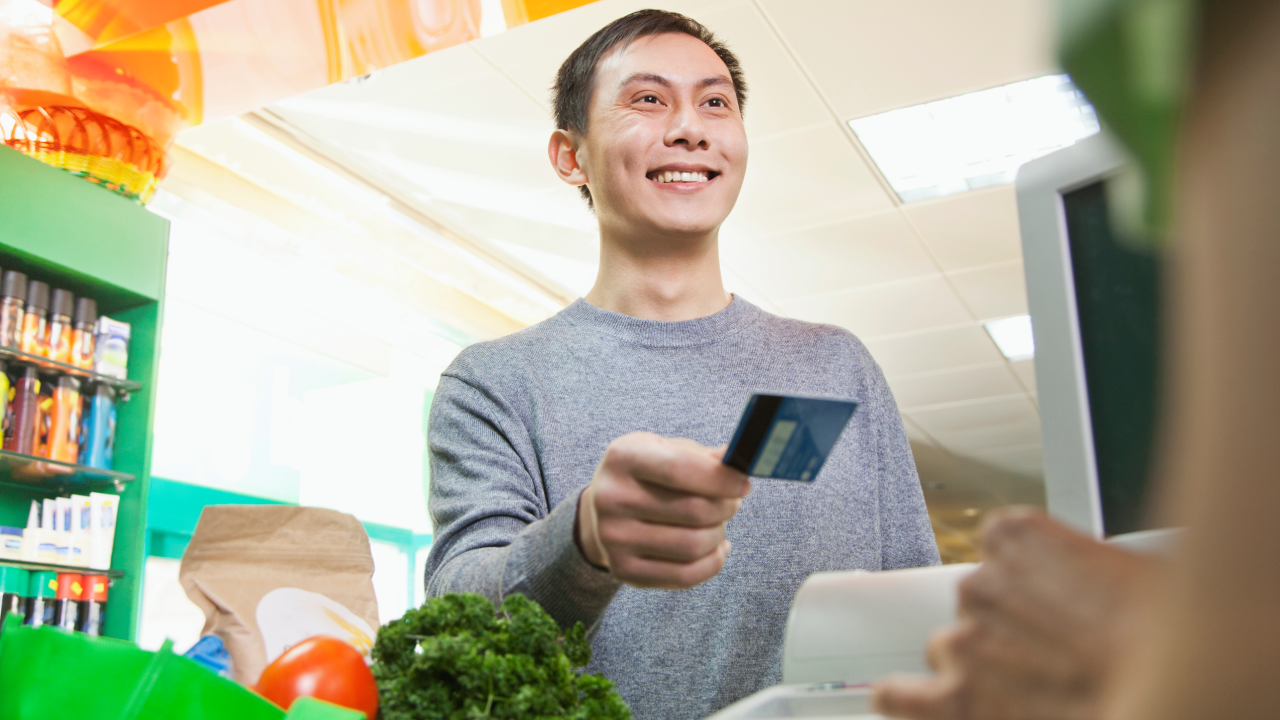 Chinese customer handing cashier credit card in grocery store