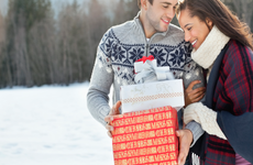 Smiling couple hugging and holding Christmas gifts in snow