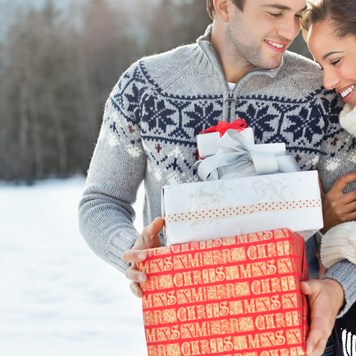 Smiling couple hugging and holding Christmas gifts in snow