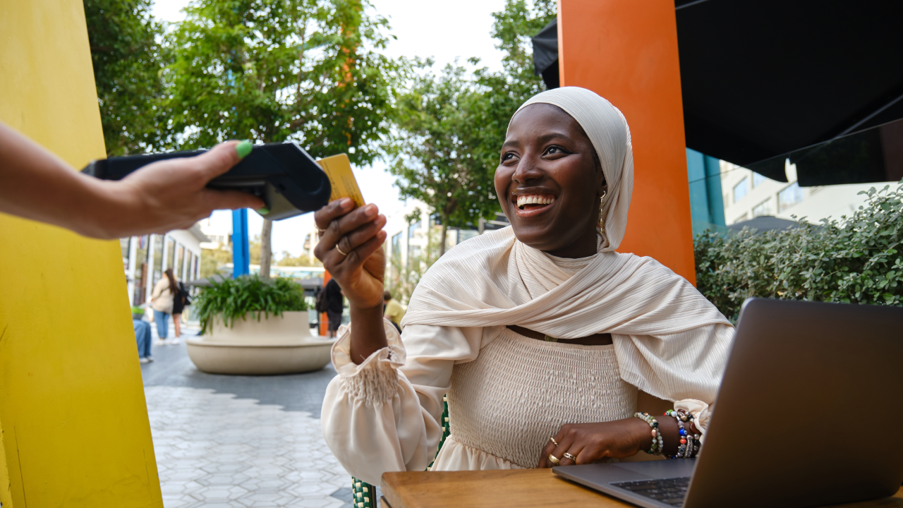 Portrait of a cheerful african muslim woman paying the bill using credit card in a cafeteria