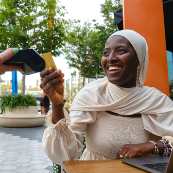 Portrait of a cheerful african muslim woman paying the bill using credit card in a cafeteria