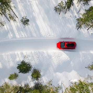 Aerial view of a red car driving through a snowy forest.
