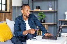 Man sitting at laptop, holding credit card, smiling