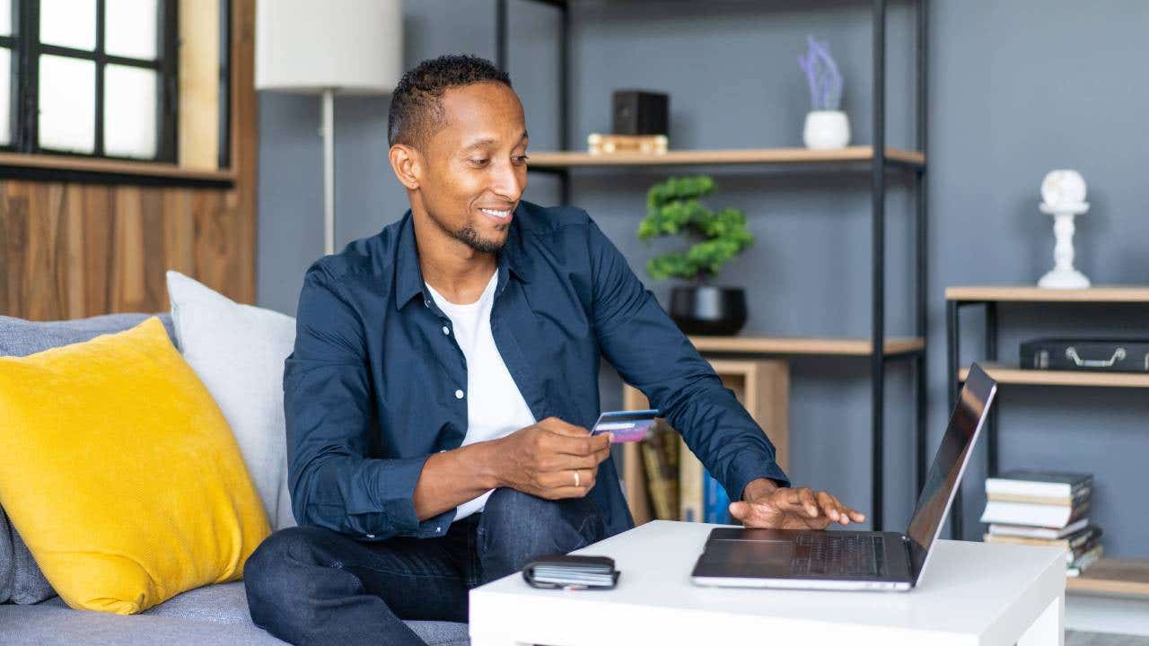 Man sitting at laptop, holding credit card, smiling