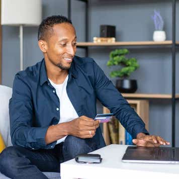 Man sitting at laptop, holding credit card, smiling