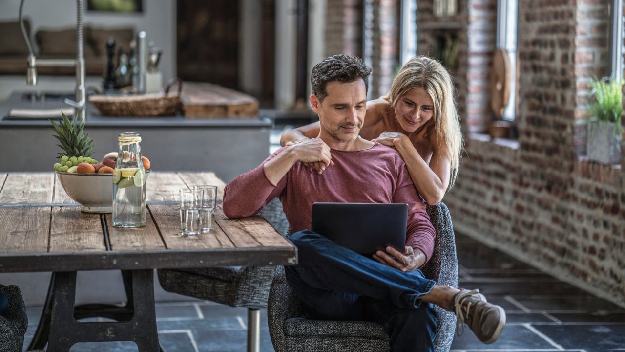 couple siting in country house kitchen, looking at laptop