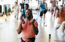 Smiling male fitness instructor practicing dumbbell exercise with men in gym - stock photo