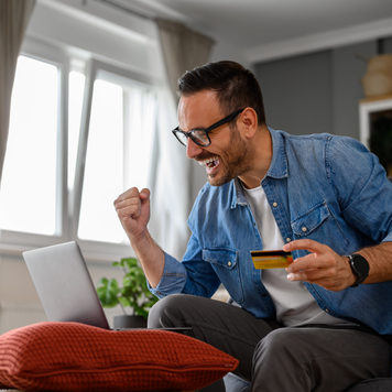 Businessman with credit card pumping fist and screaming in joy while doing online shopping on laptop