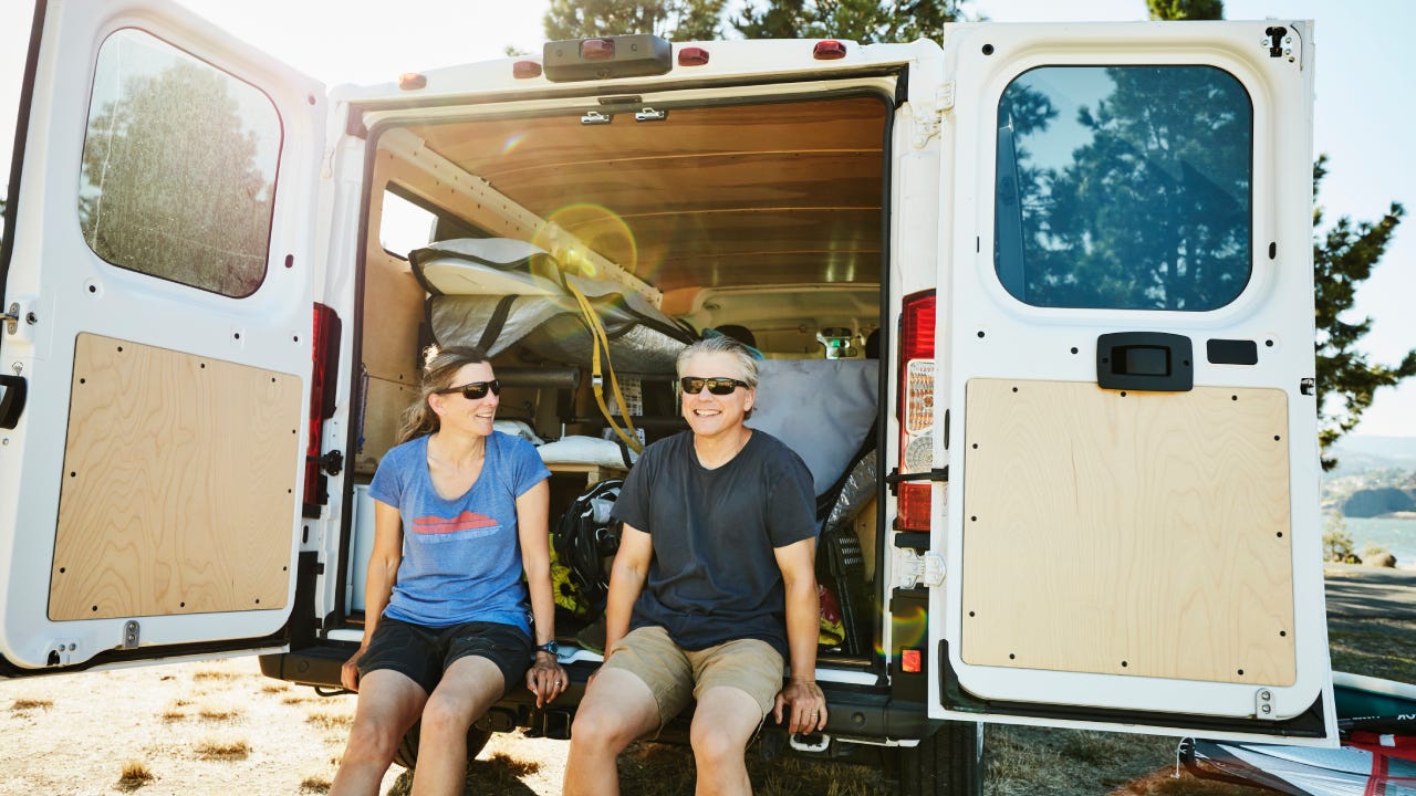 Smiling couple sitting on back of van after windsurfing on summer afternoon