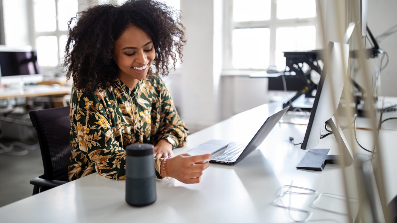 Woman with a credit card talking into a smart assistance device to do a online payment. Woman using wireless technology for online shopping.