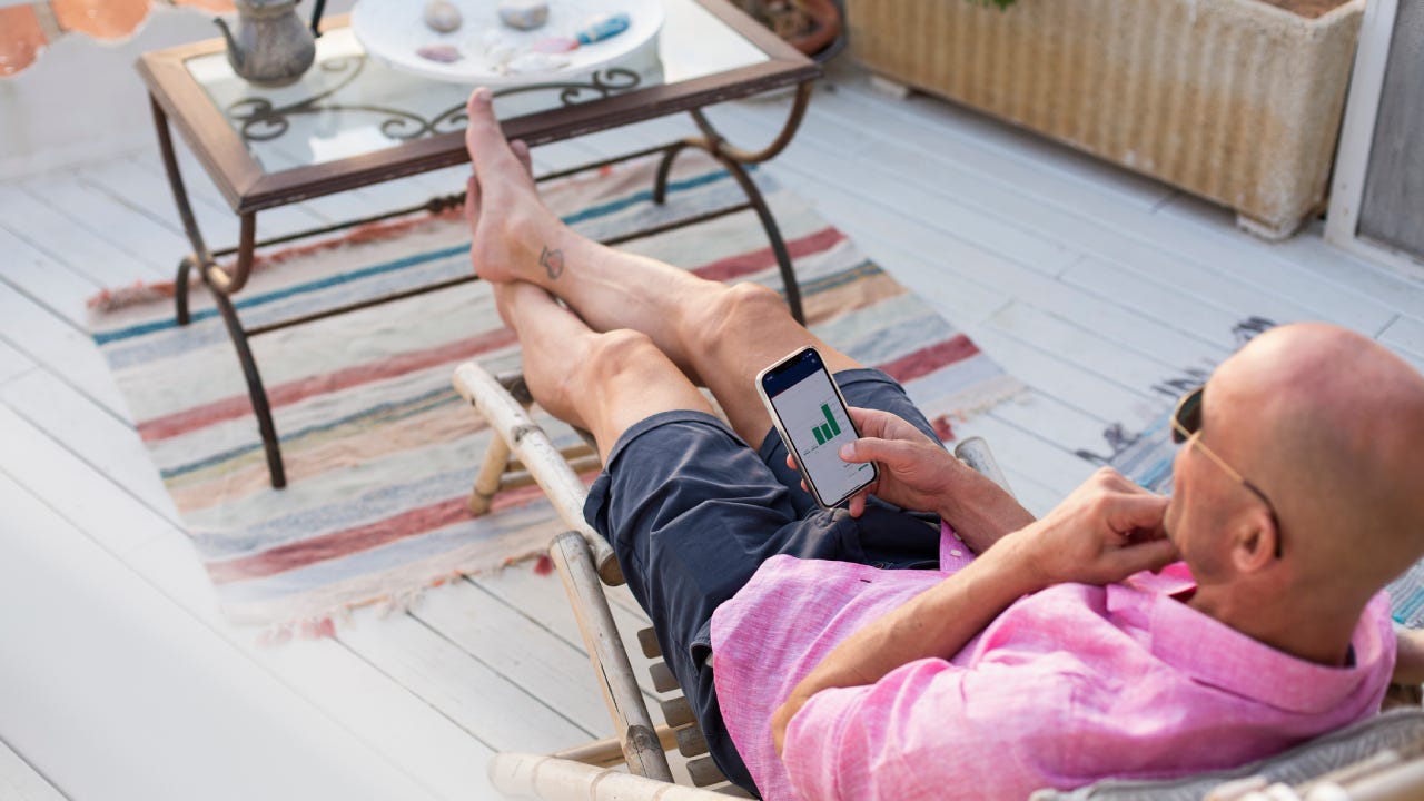 Man checking financial trading data on mobile phone while relaxing on deck chair