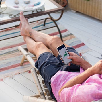 Man checking financial trading data on mobile phone while relaxing on deck chair