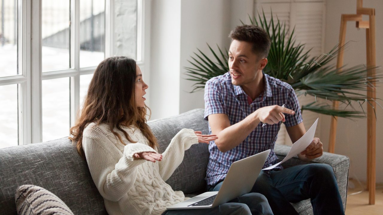 Young couple arguing about high domestic bills to pay with laptop and documents, unhappy family having conflict disagreement discussing unpaid debt or money problems sitting together on sofa at home