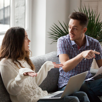 Young couple arguing about high domestic bills to pay with laptop and documents, unhappy family having conflict disagreement discussing unpaid debt or money problems sitting together on sofa at home
