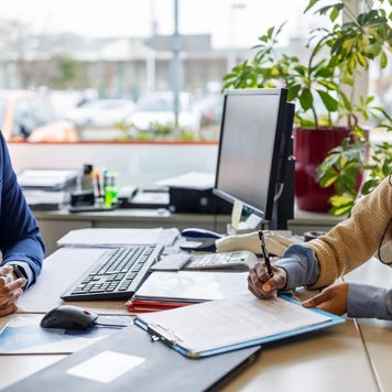 Person filling out forms at a car dealer while a salesperson guides them