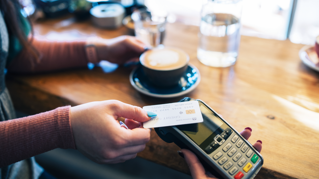 Clsoe-up of unrecognisable woman making contactless card payment in cafe.