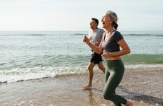 Happy mature couple laughing and running in water at beach