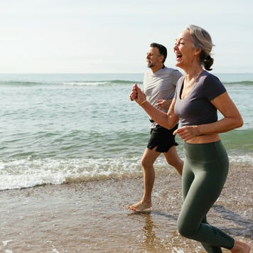 Happy mature couple laughing and running in water at beach