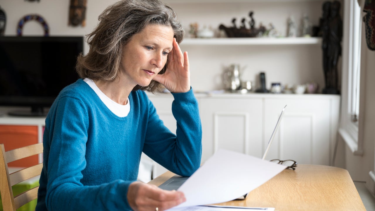 Candid side view portrait of woman studying document at desk in living room at home.