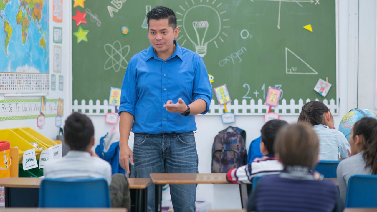 An elementary school teacher is indoors, teaching his students.