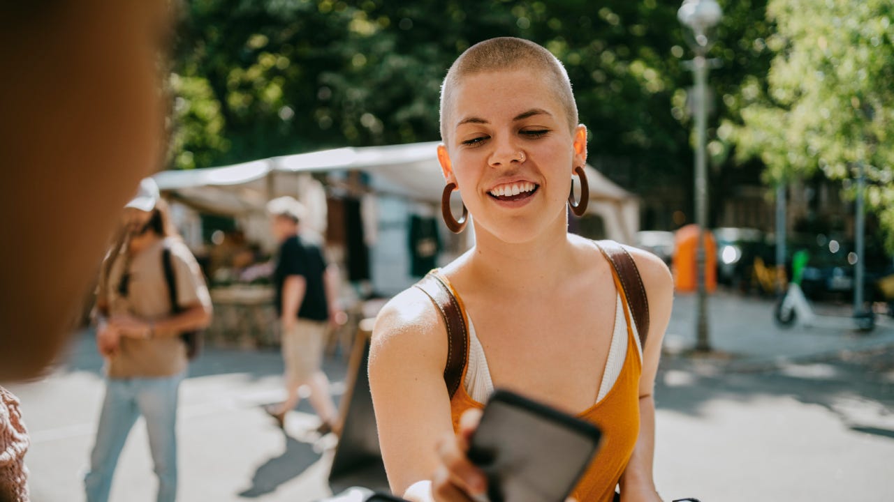 Smiling woman with shaved head paying via tap to pay while shopping at flea market