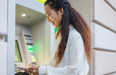 Female Person Using Mobile Phone Banking App While Standing in Front of Atm Cashpoint Machine. Nfc Online Banking Concept
