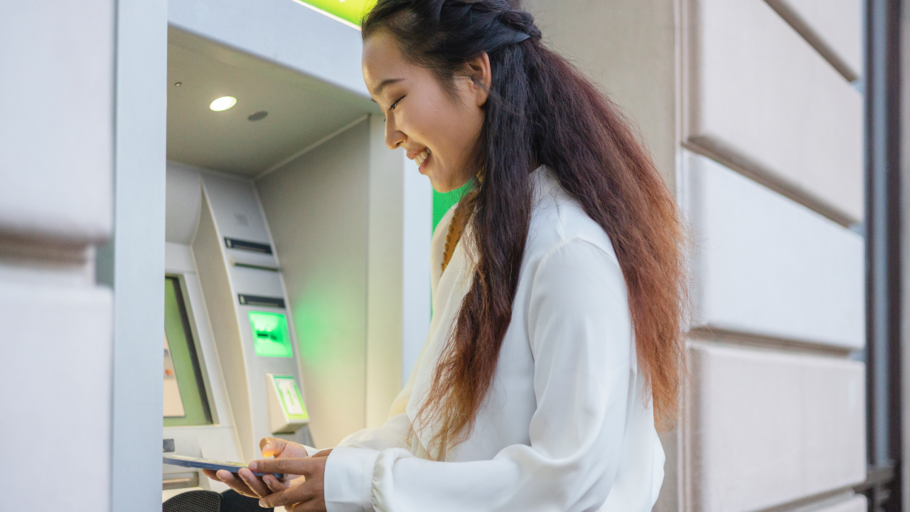 Female Person Using Mobile Phone Banking App While Standing in Front of Atm Cashpoint Machine. Nfc Online Banking Concept