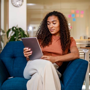 Woman sitting on a blue armchair reviewing a tablet
