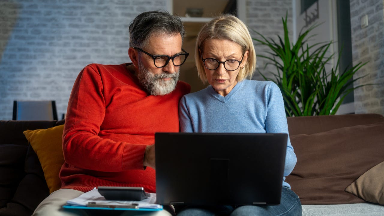 Senior couple sitting at the sofa and looking at digital tablet and recalculating their expenses