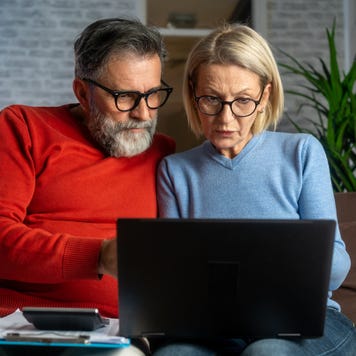 Senior couple sitting at the sofa and looking at digital tablet and recalculating their expenses