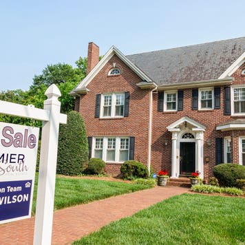 brick suburban home with for sale sign on front lawn