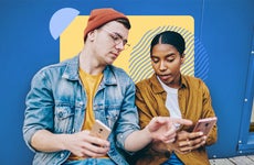 Two young adults have a conversation about something on a cellphone