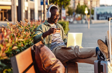 Photo of a smiling African-American man sitting on the bench and holding a credit card. E-commerce activity