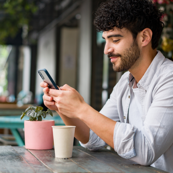 Portrait of a happy Latin American man drinking checking his cell phone at a coffee shop while drinking a cappuccino