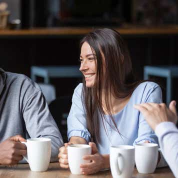 A group of millennial friends sit around a table drinking coffee.
