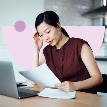 Woman studying a document and working on a laptop