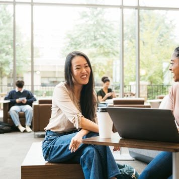 Two female university students sitting together smiling.
