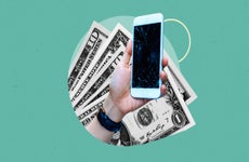 Close up of a hand holding a smartphone with a cracked screen against a background of dollar bills