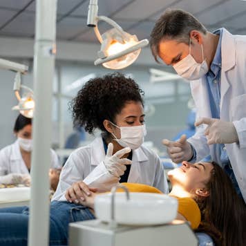 Teacher supervising a student examining a patient at dental school and explaining something to her